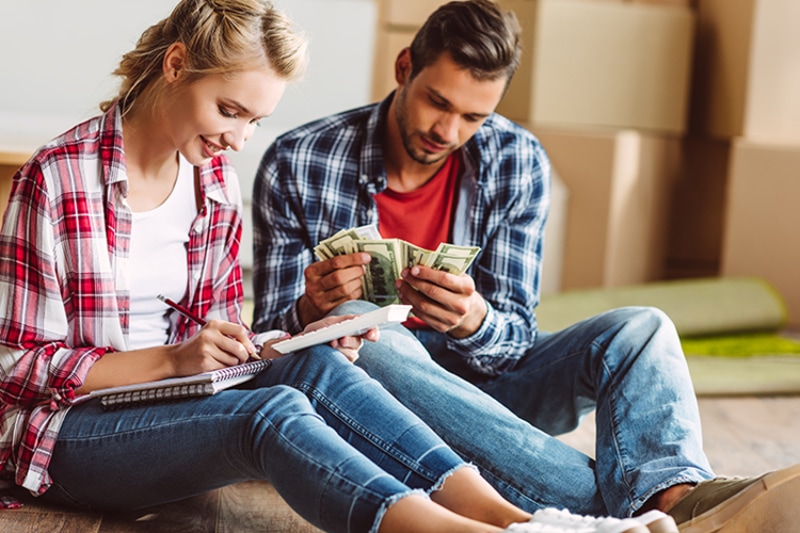 young couple counting money while sitting on floor in new apartment.